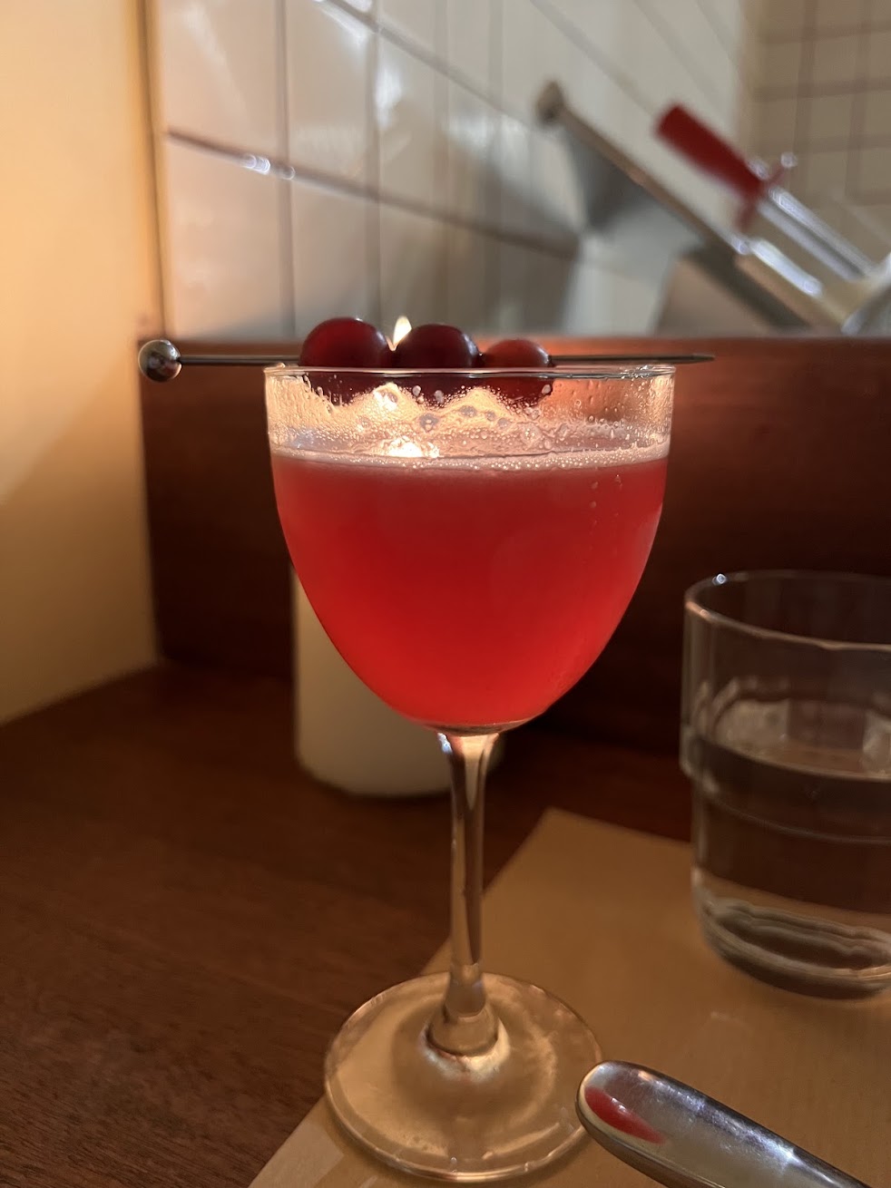 A bright red Enzoni cocktail garnished with grapes at Tiella